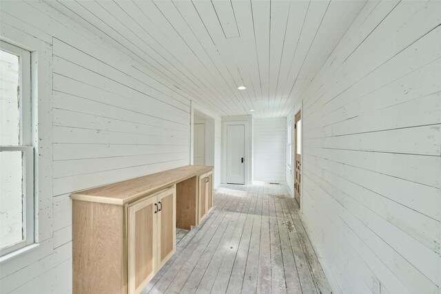 hall with light wood-type flooring, wooden ceiling, and wooden walls