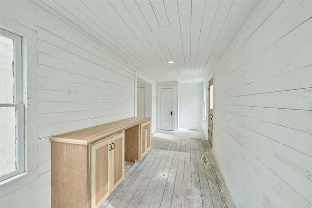 hall featuring light wood-type flooring, wood ceiling, and wooden walls