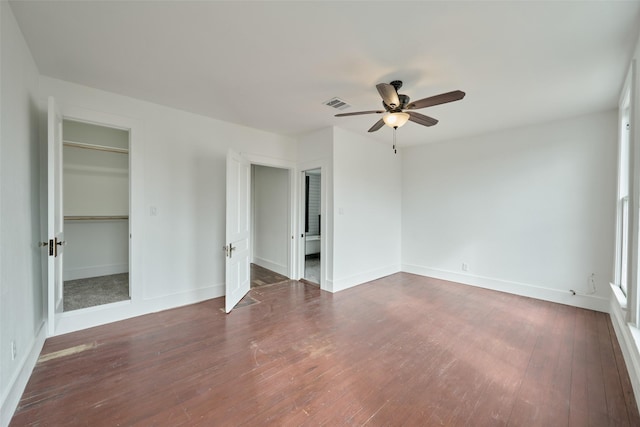 unfurnished bedroom with a spacious closet, ceiling fan, a closet, and dark hardwood / wood-style floors