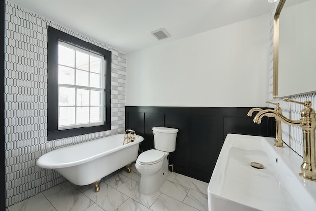 bathroom featuring marble finish floor, visible vents, toilet, vanity, and a freestanding tub