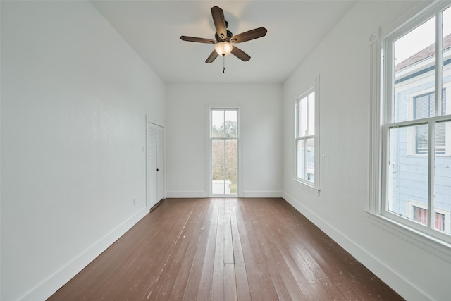 empty room with dark wood-type flooring, a ceiling fan, and baseboards