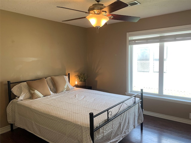 bedroom with a ceiling fan, wood finished floors, visible vents, and baseboards