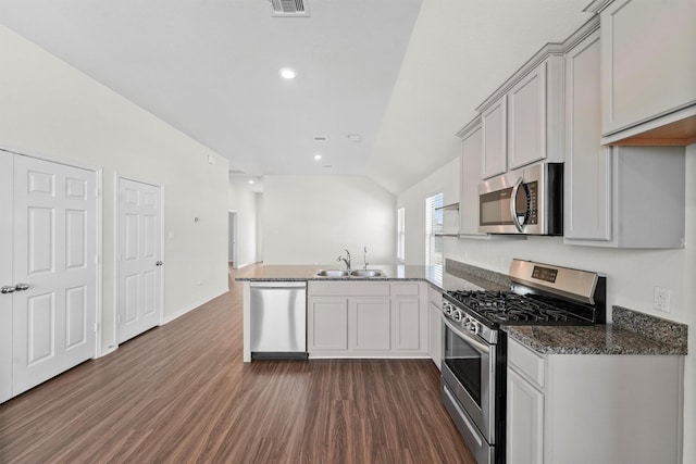 kitchen featuring kitchen peninsula, appliances with stainless steel finishes, dark stone counters, vaulted ceiling, and sink