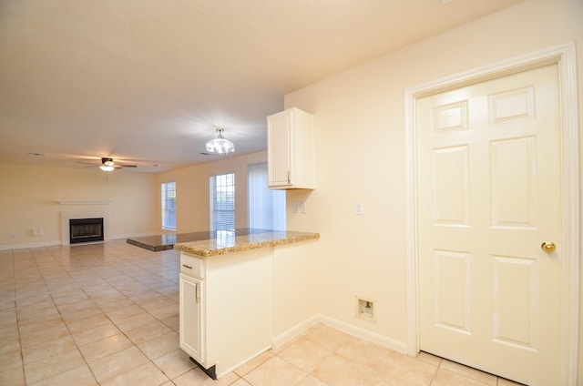 kitchen with kitchen peninsula, light stone counters, ceiling fan, light tile patterned floors, and white cabinetry