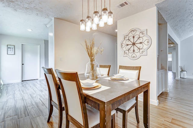 dining space with a textured ceiling, an inviting chandelier, and light hardwood / wood-style flooring