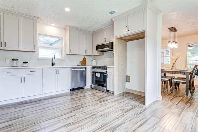 kitchen featuring plenty of natural light, sink, appliances with stainless steel finishes, decorative light fixtures, and white cabinetry