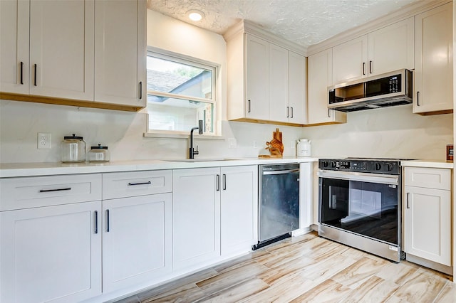 kitchen featuring sink, light hardwood / wood-style floors, a textured ceiling, white cabinets, and appliances with stainless steel finishes