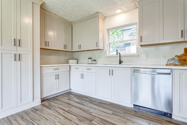 kitchen featuring a textured ceiling, light wood-type flooring, stainless steel dishwasher, and sink