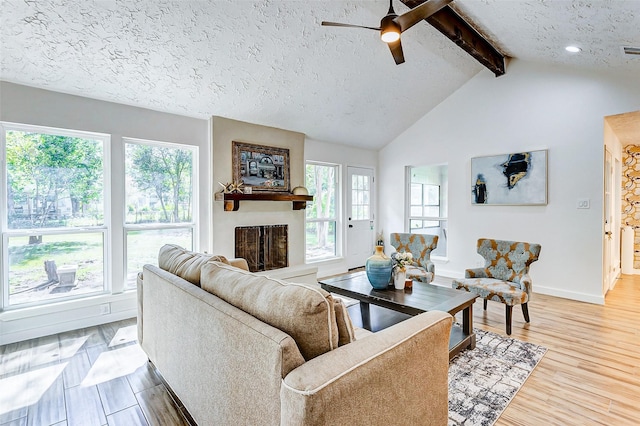 living room with vaulted ceiling with beams, ceiling fan, a textured ceiling, and light hardwood / wood-style flooring