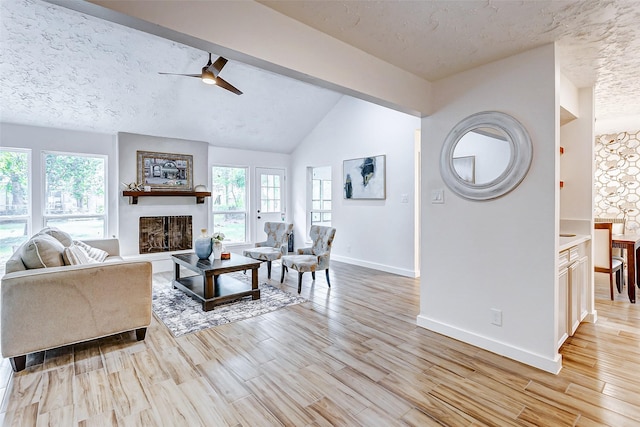 living room featuring vaulted ceiling with beams, ceiling fan, light wood-type flooring, and a textured ceiling