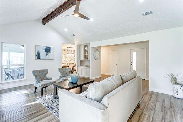 living room with lofted ceiling with beams, a textured ceiling, and light wood-type flooring