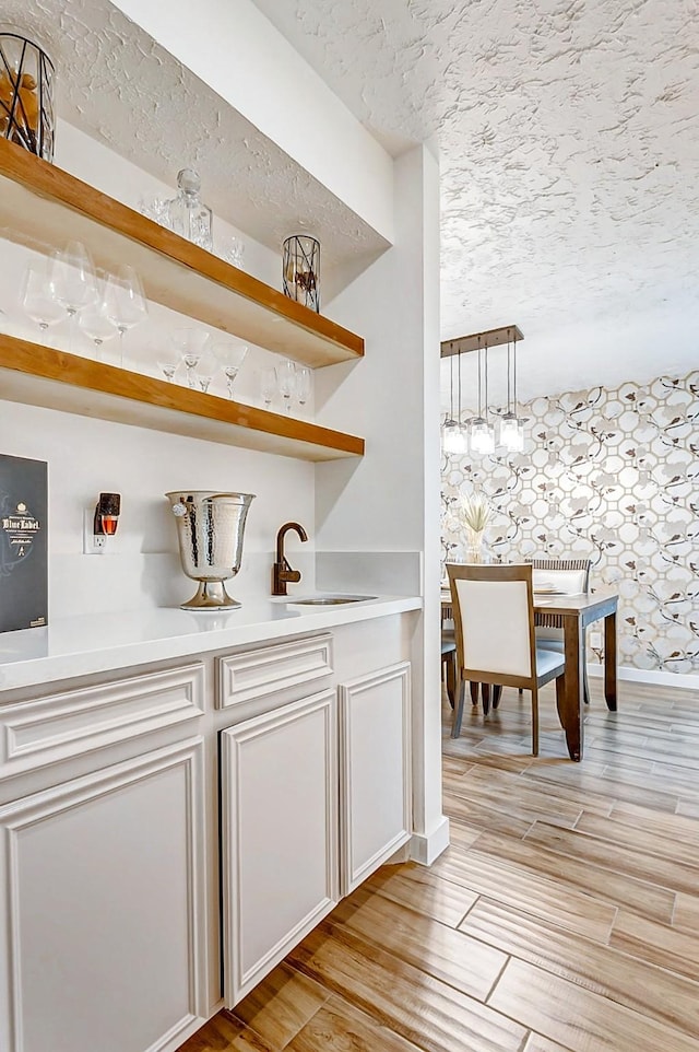 bar with white cabinets, light hardwood / wood-style floors, sink, and hanging light fixtures