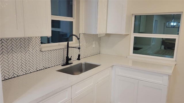 kitchen featuring a notable chandelier, white cabinetry, sink, and tasteful backsplash