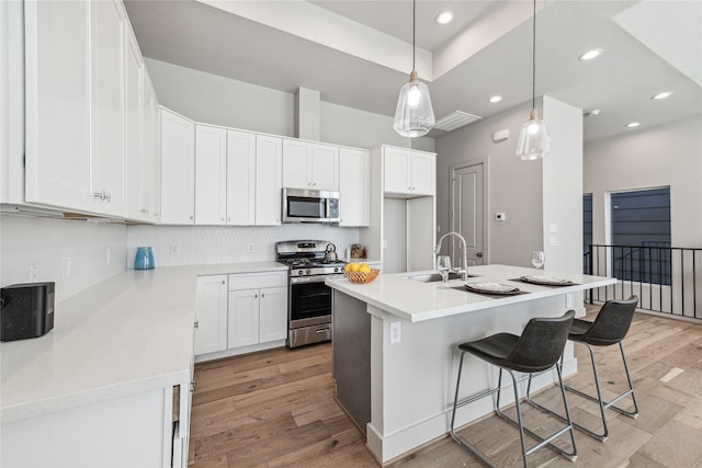 kitchen featuring appliances with stainless steel finishes, sink, white cabinets, hanging light fixtures, and an island with sink