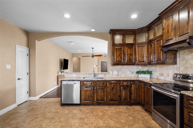 kitchen with light stone countertops, sink, ceiling fan, exhaust hood, and appliances with stainless steel finishes