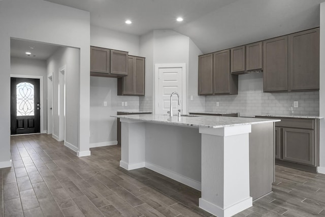 kitchen with dark hardwood / wood-style flooring, sink, an island with sink, and vaulted ceiling