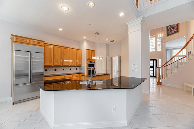 kitchen featuring light tile patterned floors, a center island with sink, stainless steel appliances, and ornate columns