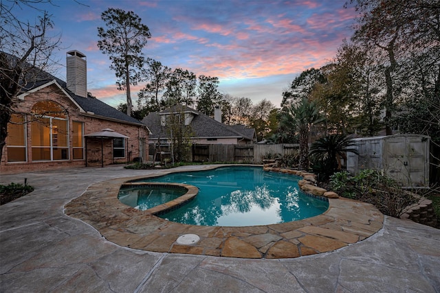 pool at dusk with a patio and an in ground hot tub