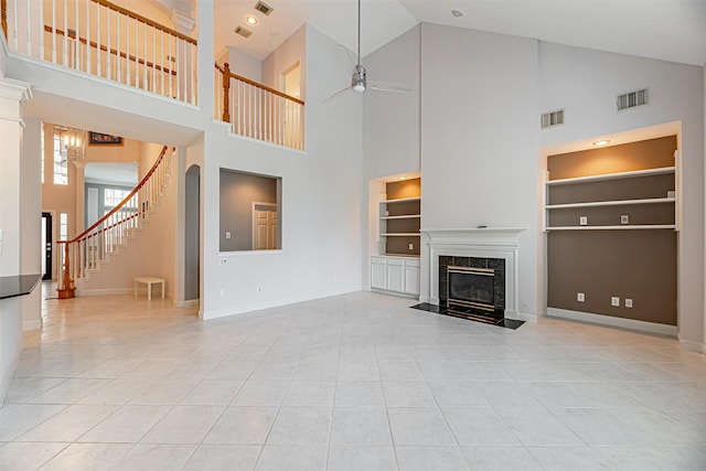 unfurnished living room with a high ceiling, built in shelves, a premium fireplace, ceiling fan, and light tile patterned floors