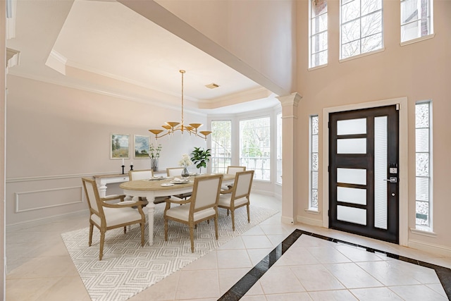 foyer entrance featuring an inviting chandelier, light tile patterned floors, a raised ceiling, and decorative columns