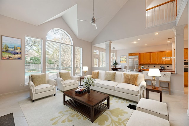 tiled living room featuring ceiling fan, sink, high vaulted ceiling, and decorative columns