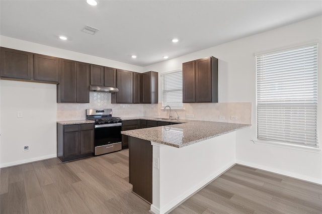 kitchen featuring sink, stainless steel gas range, light stone counters, kitchen peninsula, and light hardwood / wood-style floors