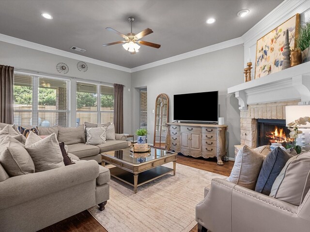 living room featuring crown molding, hardwood / wood-style floors, ceiling fan, and a brick fireplace