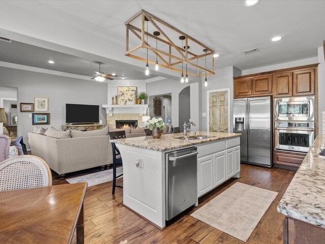 kitchen with appliances with stainless steel finishes, light stone counters, sink, a center island with sink, and white cabinets