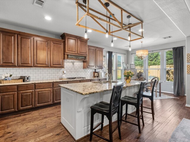 kitchen with sink, an inviting chandelier, pendant lighting, a kitchen island with sink, and a breakfast bar