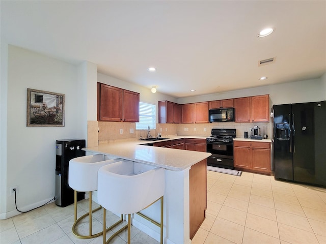 kitchen with kitchen peninsula, tasteful backsplash, sink, black appliances, and a breakfast bar area