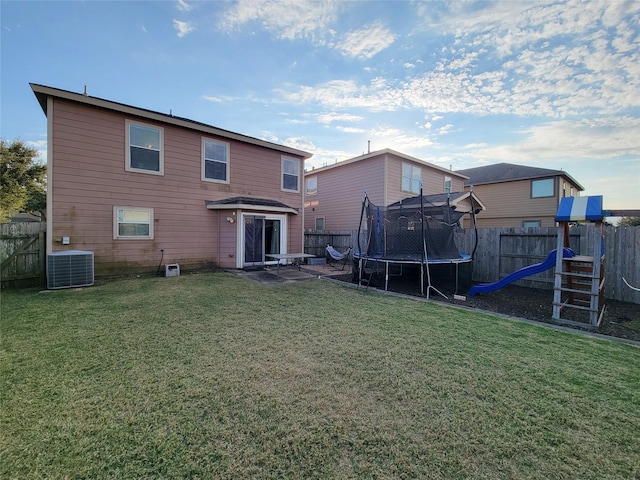 rear view of house with central AC unit, a playground, a trampoline, and a lawn