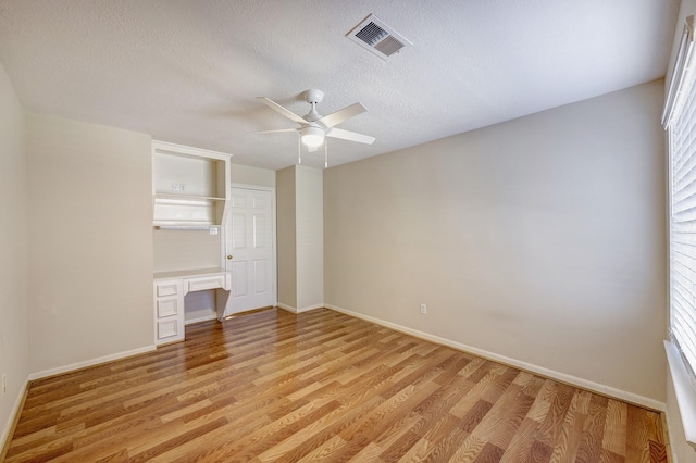 unfurnished bedroom with light wood-type flooring, a closet, ceiling fan, and built in desk