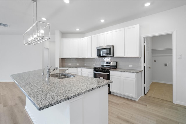 kitchen with stainless steel appliances, sink, decorative light fixtures, white cabinets, and an island with sink