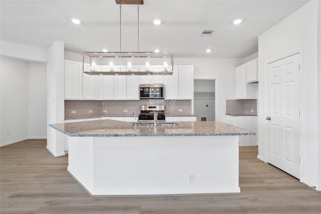 kitchen featuring a center island with sink, pendant lighting, white cabinets, and stainless steel appliances