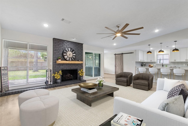 living room featuring light hardwood / wood-style flooring, vaulted ceiling, ceiling fan, a barn door, and a fireplace