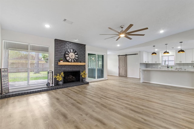 unfurnished living room featuring ceiling fan, a barn door, light hardwood / wood-style floors, vaulted ceiling, and a fireplace