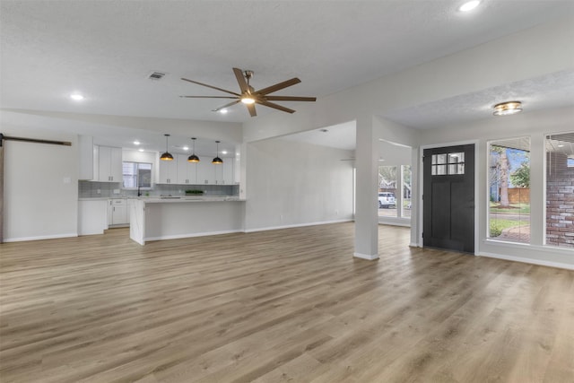 unfurnished living room featuring a barn door, ceiling fan, lofted ceiling, and light wood-type flooring