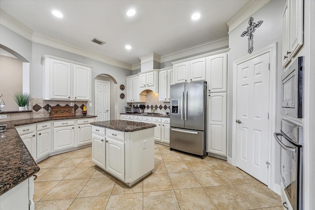 kitchen with decorative backsplash, dark stone countertops, appliances with stainless steel finishes, a kitchen island, and white cabinetry