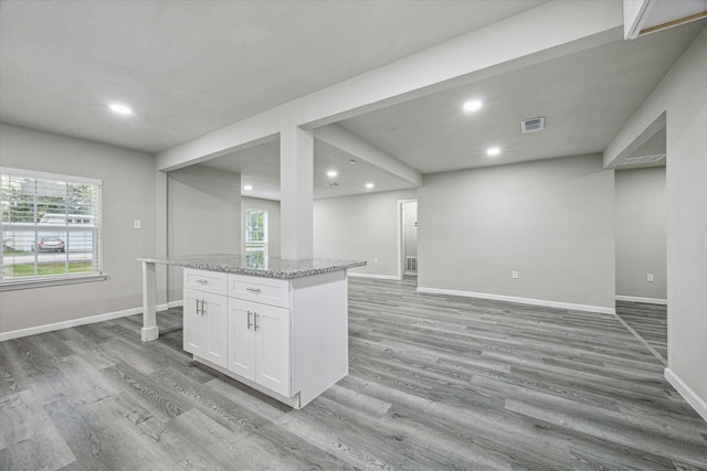 kitchen featuring light stone countertops, white cabinets, light wood-type flooring, and a kitchen island