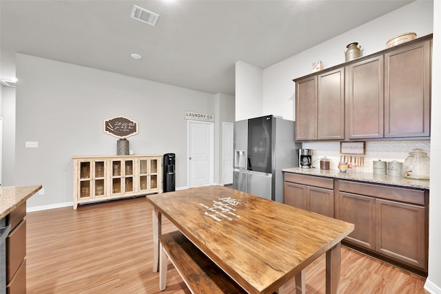 kitchen with light stone countertops, stainless steel refrigerator with ice dispenser, light hardwood / wood-style floors, and dark brown cabinets