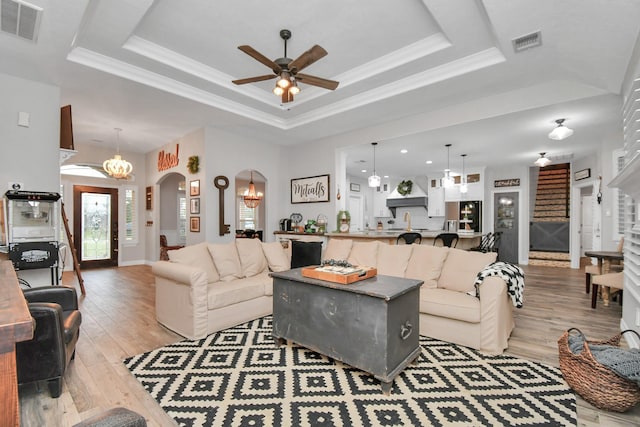 living room featuring ceiling fan with notable chandelier, light wood-type flooring, a tray ceiling, and ornamental molding