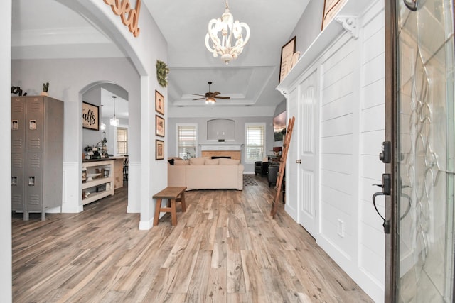 foyer with light wood-type flooring, ceiling fan with notable chandelier, and a tray ceiling