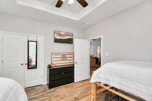 bedroom with a raised ceiling, crown molding, hardwood / wood-style flooring, ceiling fan, and a closet