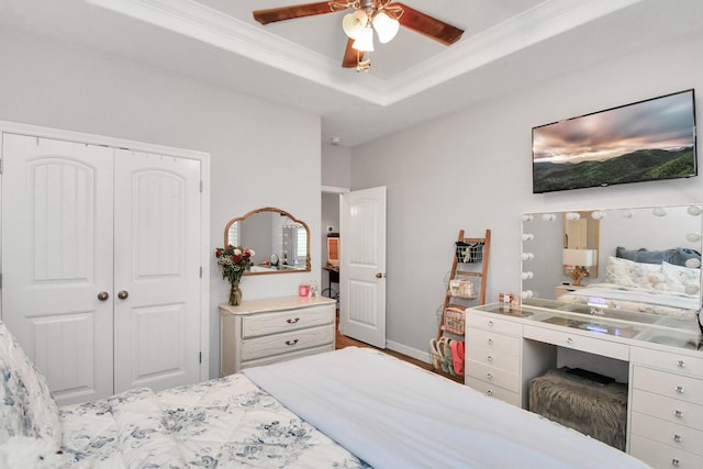 bedroom with ceiling fan, a raised ceiling, ornamental molding, and a closet