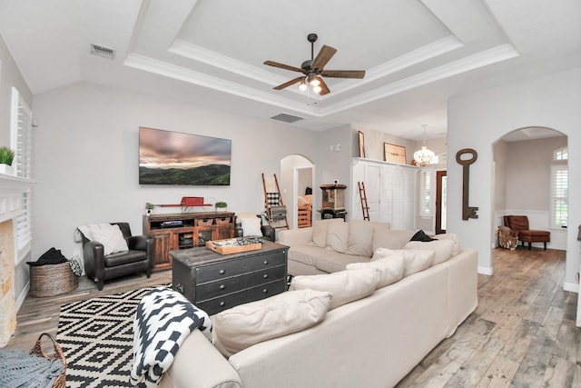 living room featuring a brick fireplace, ceiling fan with notable chandelier, a raised ceiling, crown molding, and hardwood / wood-style floors