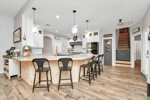 kitchen featuring kitchen peninsula, stainless steel fridge, white cabinetry, and custom range hood