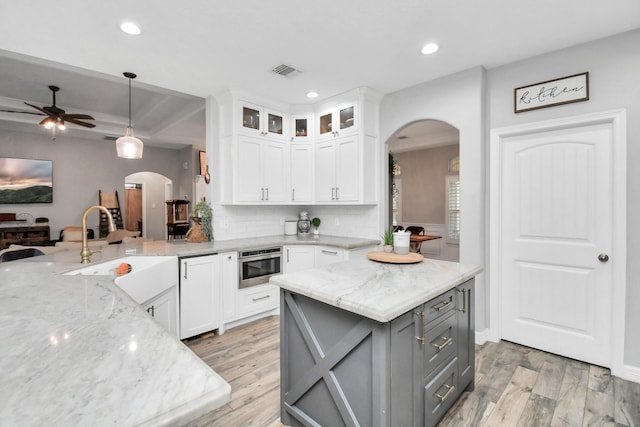 kitchen featuring light stone counters, stainless steel oven, white cabinets, and decorative light fixtures