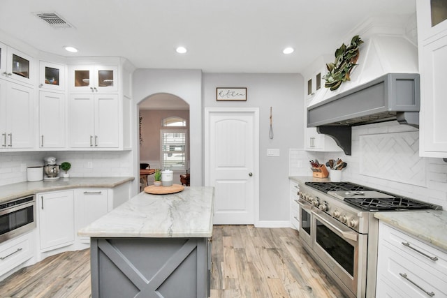 kitchen featuring white cabinets, range with two ovens, a kitchen island, and light stone counters