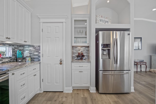 kitchen featuring stainless steel fridge, light stone countertops, white cabinetry, and tasteful backsplash