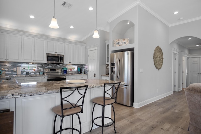 kitchen featuring white cabinets, hanging light fixtures, decorative backsplash, light stone countertops, and stainless steel appliances